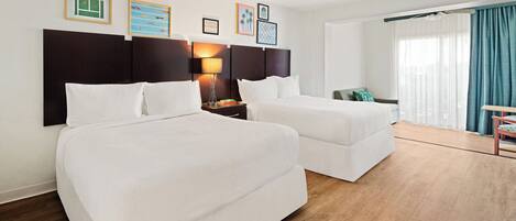 A hotel room with two beds, a nightstand with a lamp, and a view of the outdoors through a window with curtains.