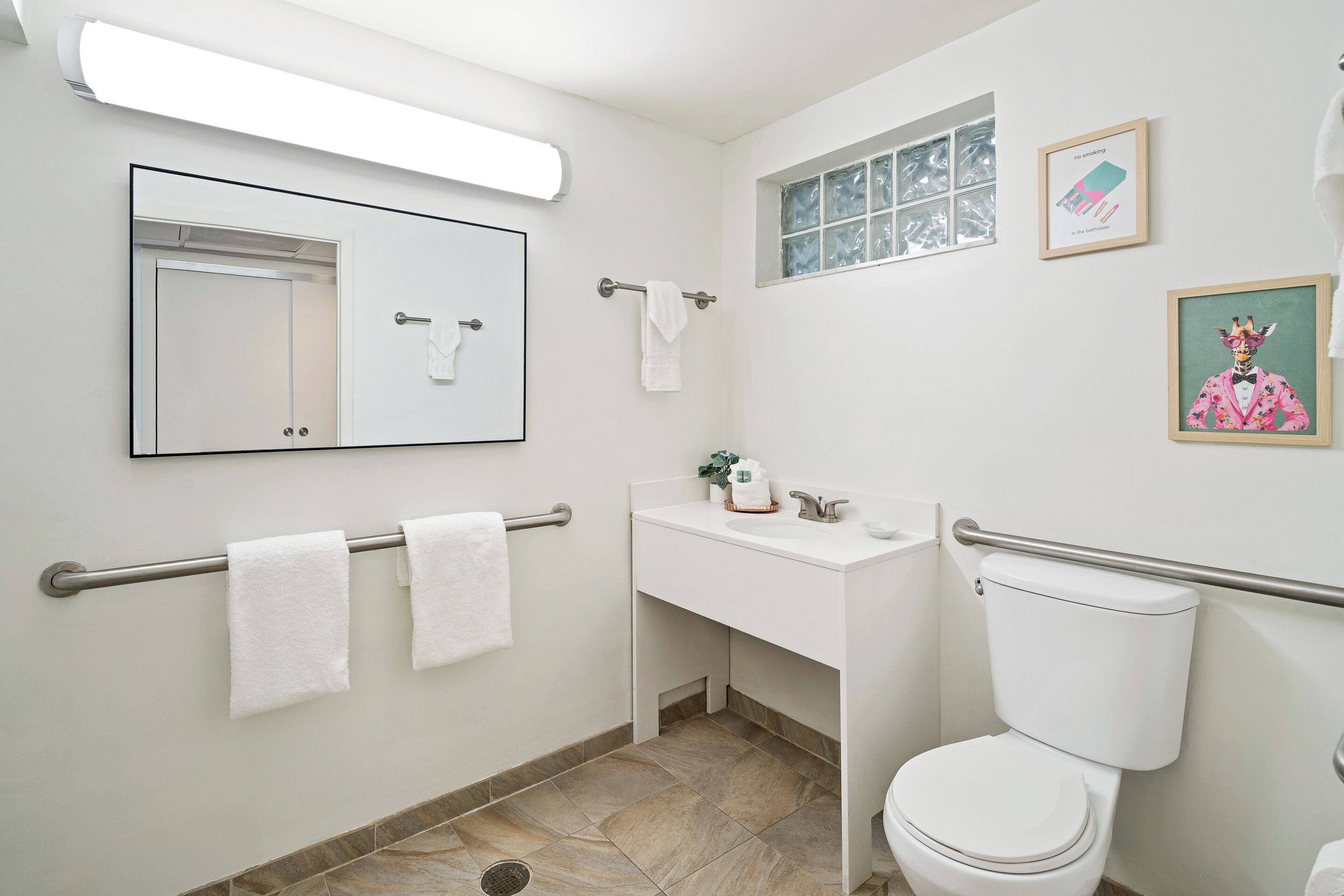 A bathroom with a white sink, toilet, and mirror. There are two towels hanging on a towel rack.