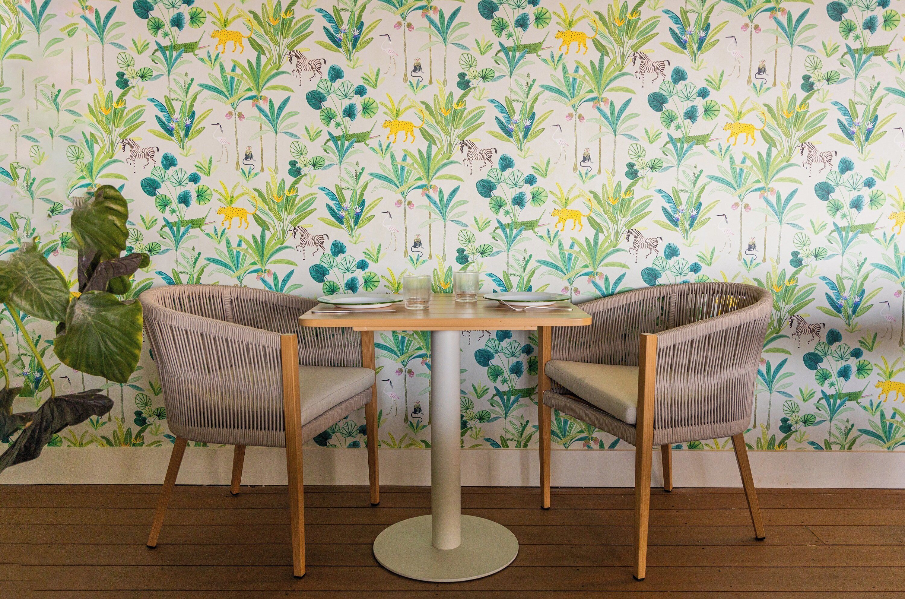 Een eetgedeelte met een ronde tafel en twee stoelen, behang met een patroon en een houten vloer.