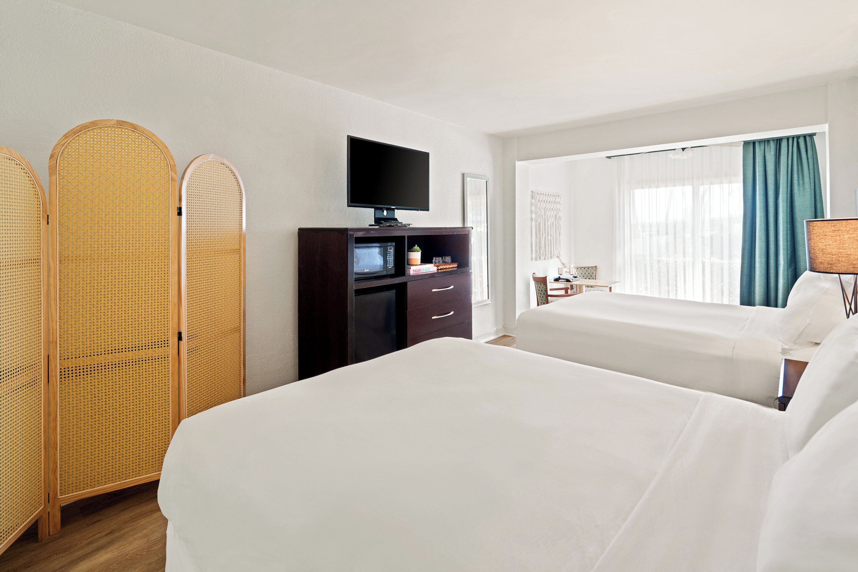 Quarto de hotel com duas camas, televisão, minibar e janela com cortinas.