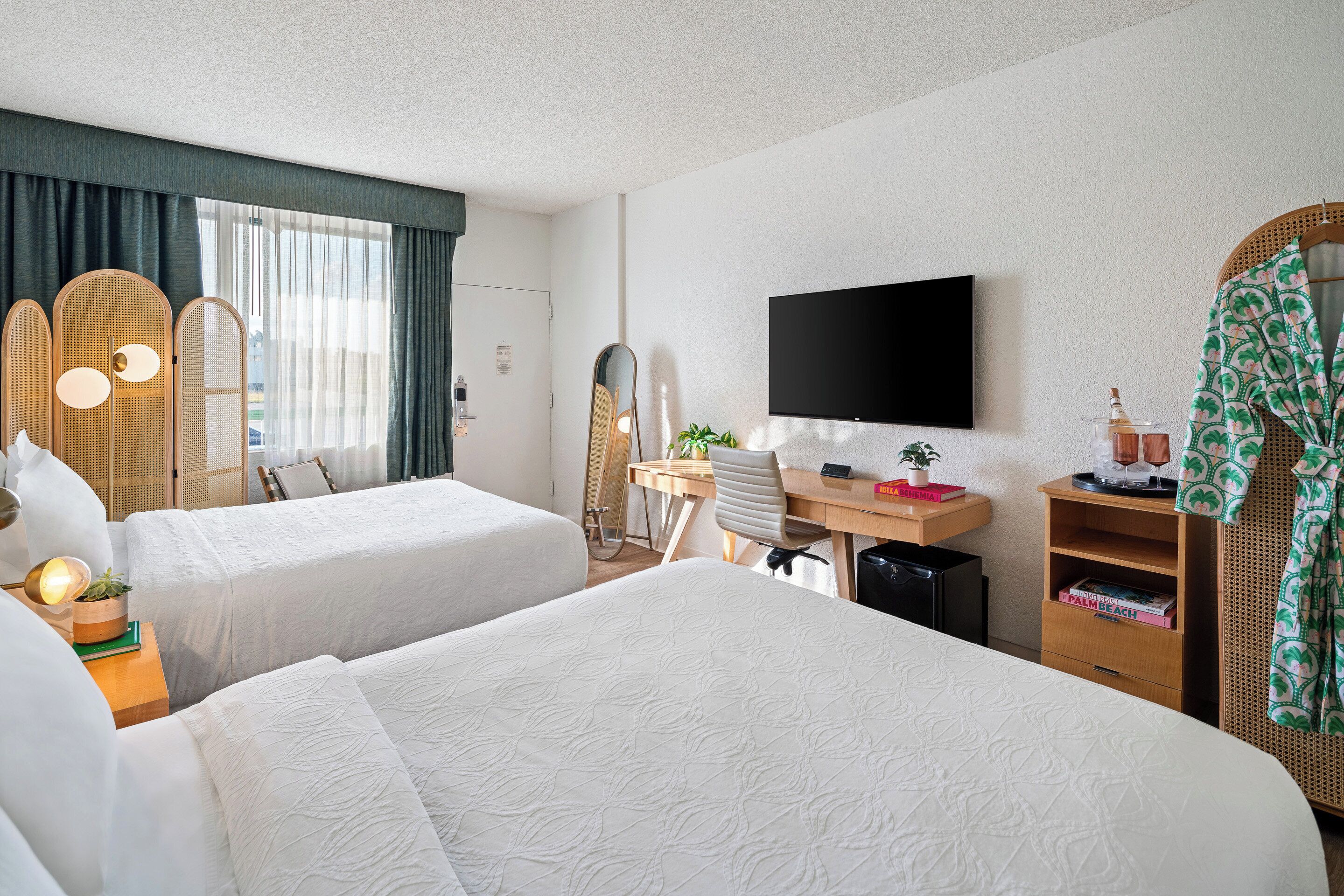 Una habitación de hotel con dos camas, un escritorio, un televisor y un espejo.