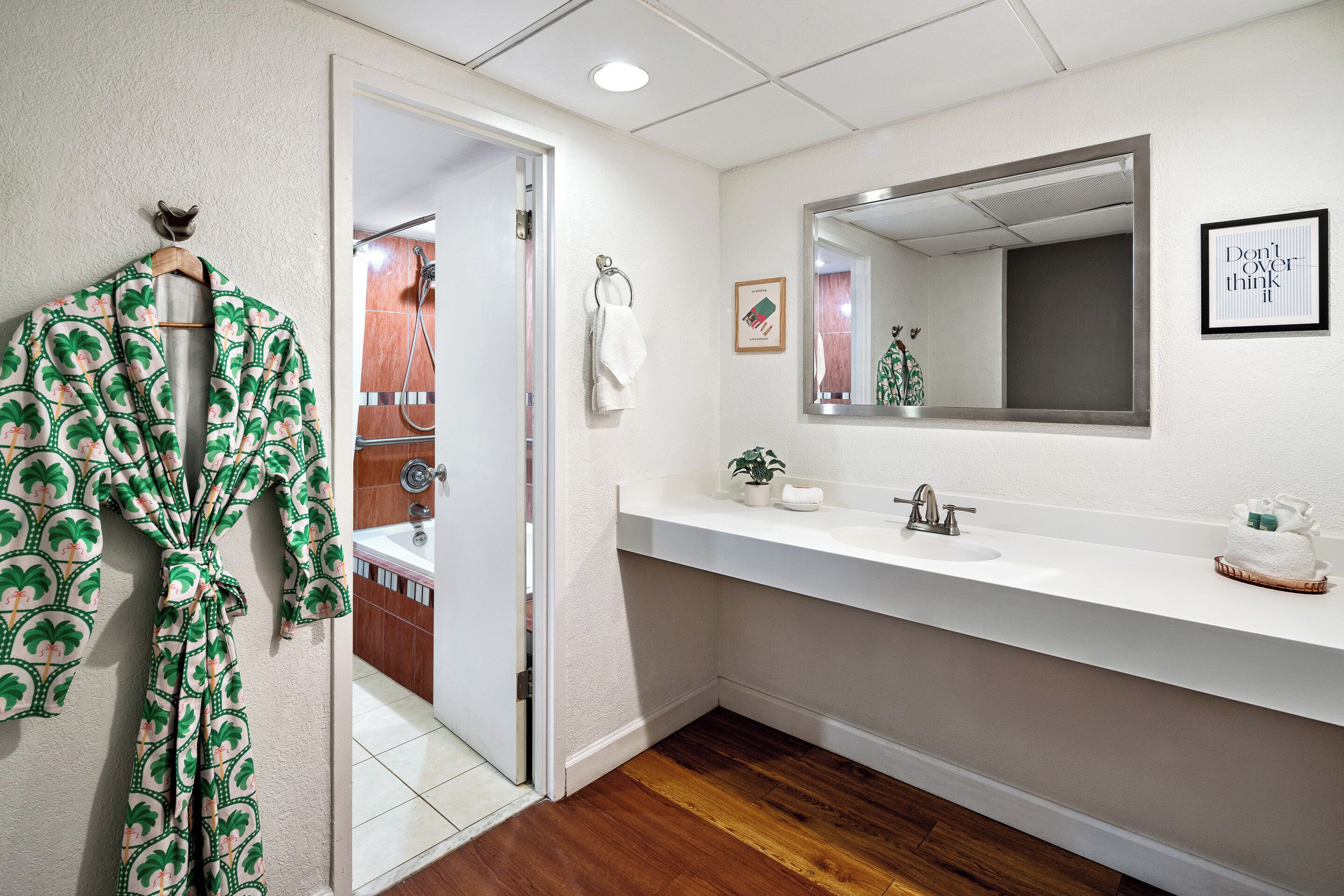 A bathroom with a wooden floor, a white sink, a mirror, and a robe hanging on a hook.