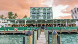 A waterfront building with a green facade and multiple balconies, a dock leading to it, and palm trees in the background. - Palm Tree Club Miami Hotel (North Bay Village)