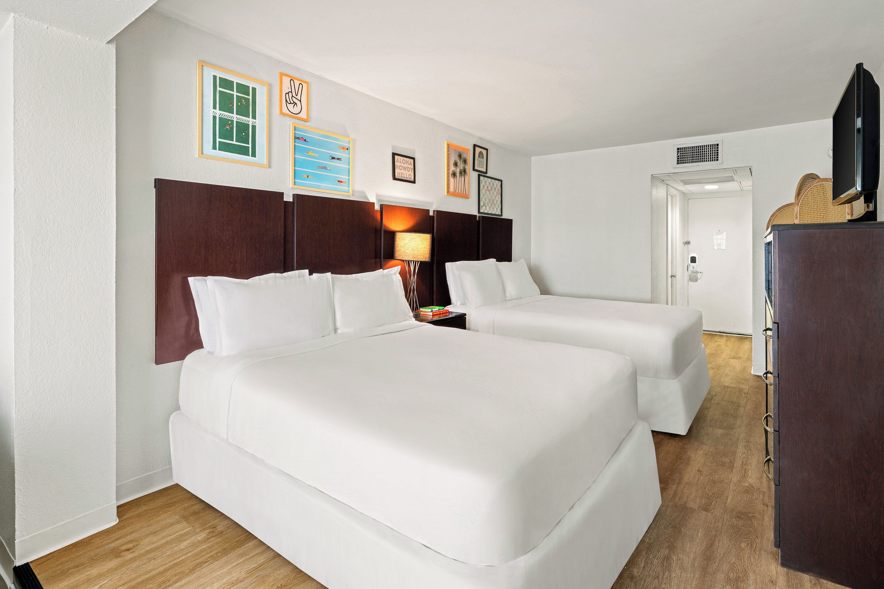 Ein Hotelzimmer mit zwei Betten, einem Nachttisch mit Lampe, einem Kleiderschrank und Wanddekorationen.