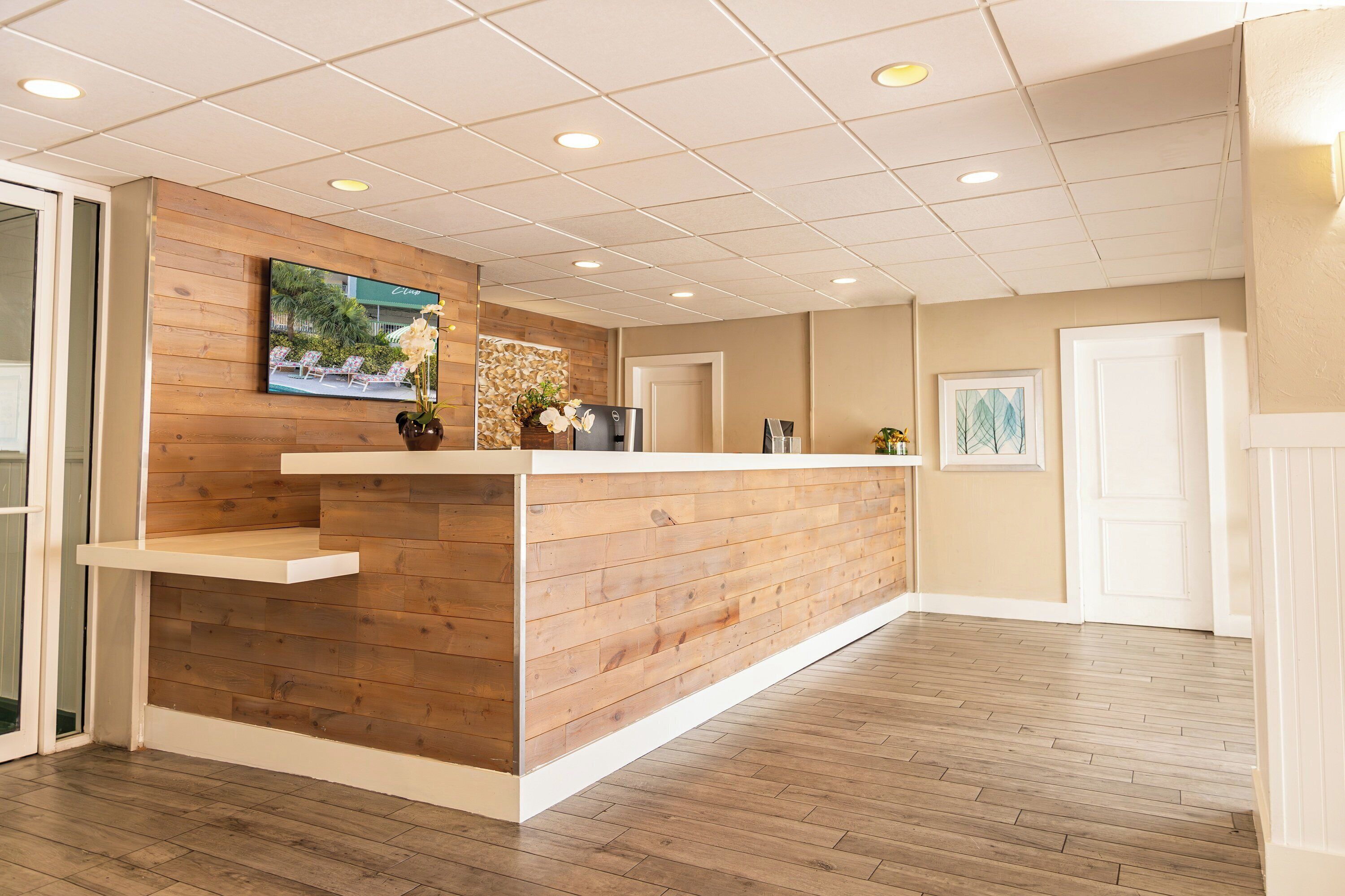 A reception area with a wooden reception desk, a television mounted on the wall, and a framed picture on the wall.