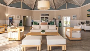A spacious, well-lit room with a high ceiling and wooden beams, featuring a central seating area with a sofa and ottomans, a gift shop, and a reception desk. - Palm Tree Club Miami Hotel (North Bay Village)