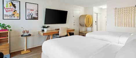 A hotel room with a large bed, a desk with a computer, a TV, and two posters on the wall.