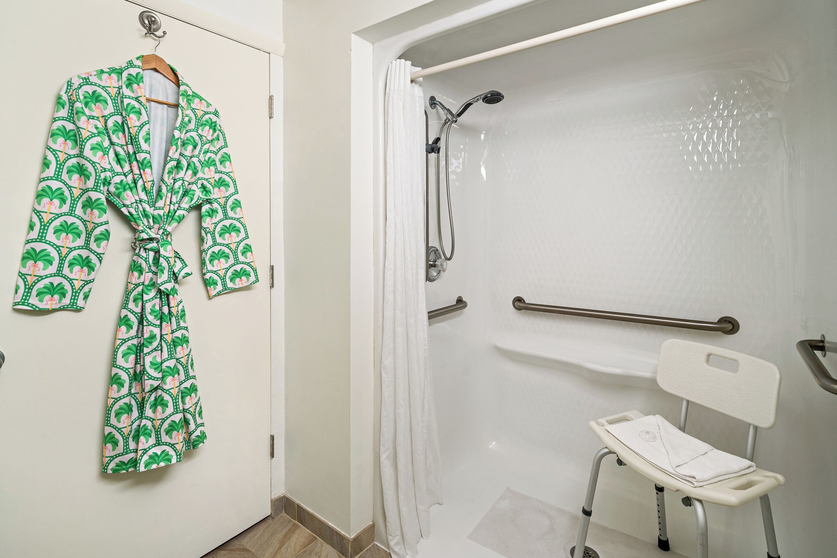 Un baño con ducha, una silla blanca y una bata colgada en la puerta.