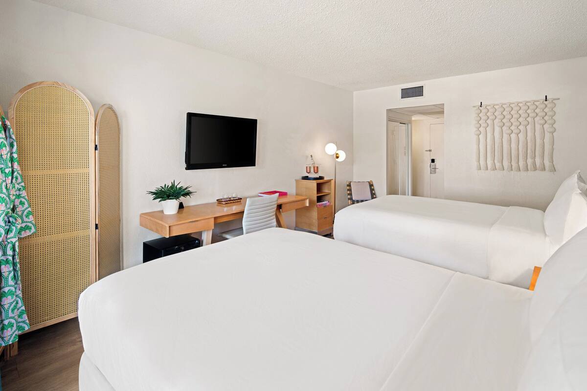 A hotel room with two beds, a desk with a computer, a TV, and a plant.