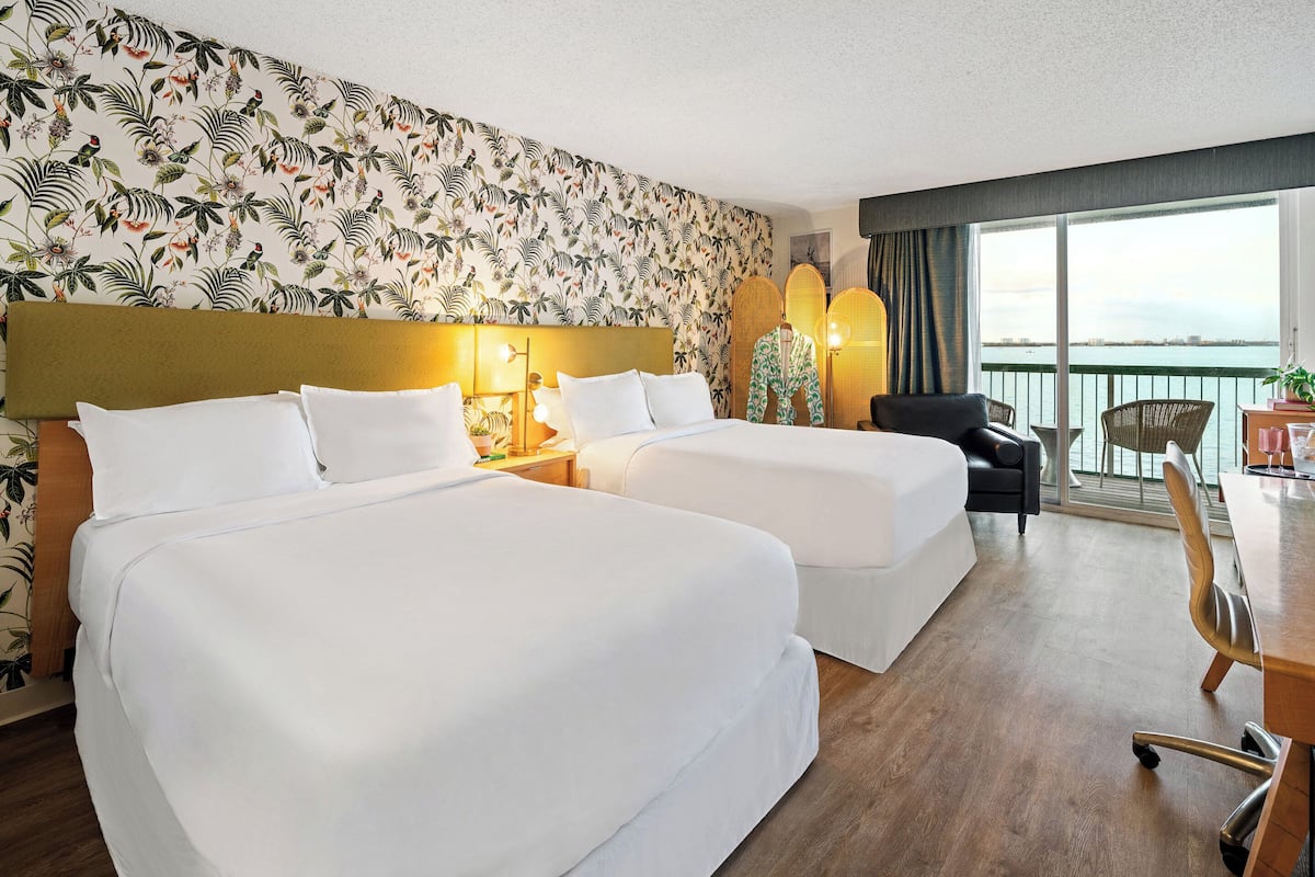 A hotel room with two beds, a desk, and a chair.