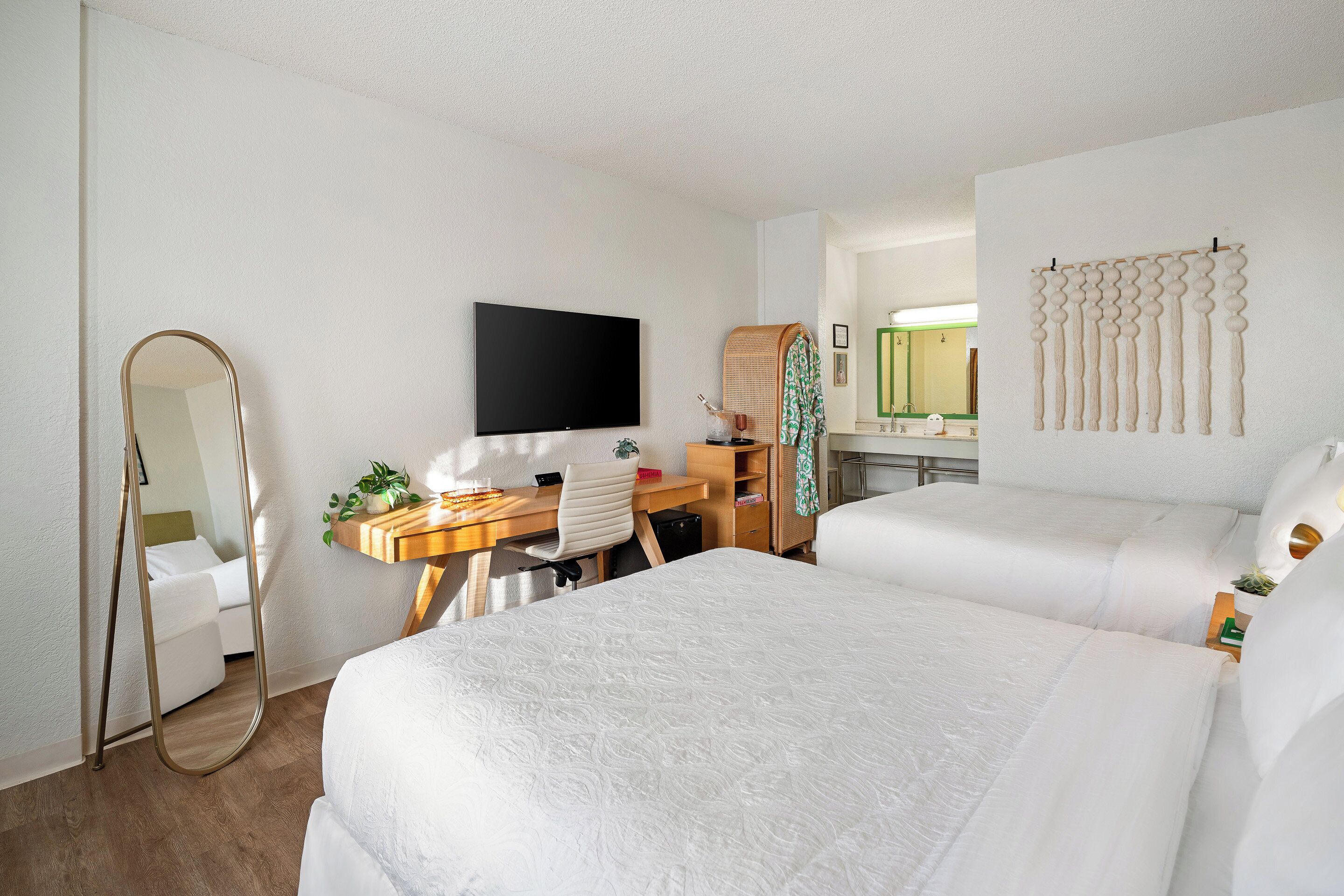 A hotel room with two beds, a desk with a chair, a television, a mirror, and a wall-mounted decorative item.
