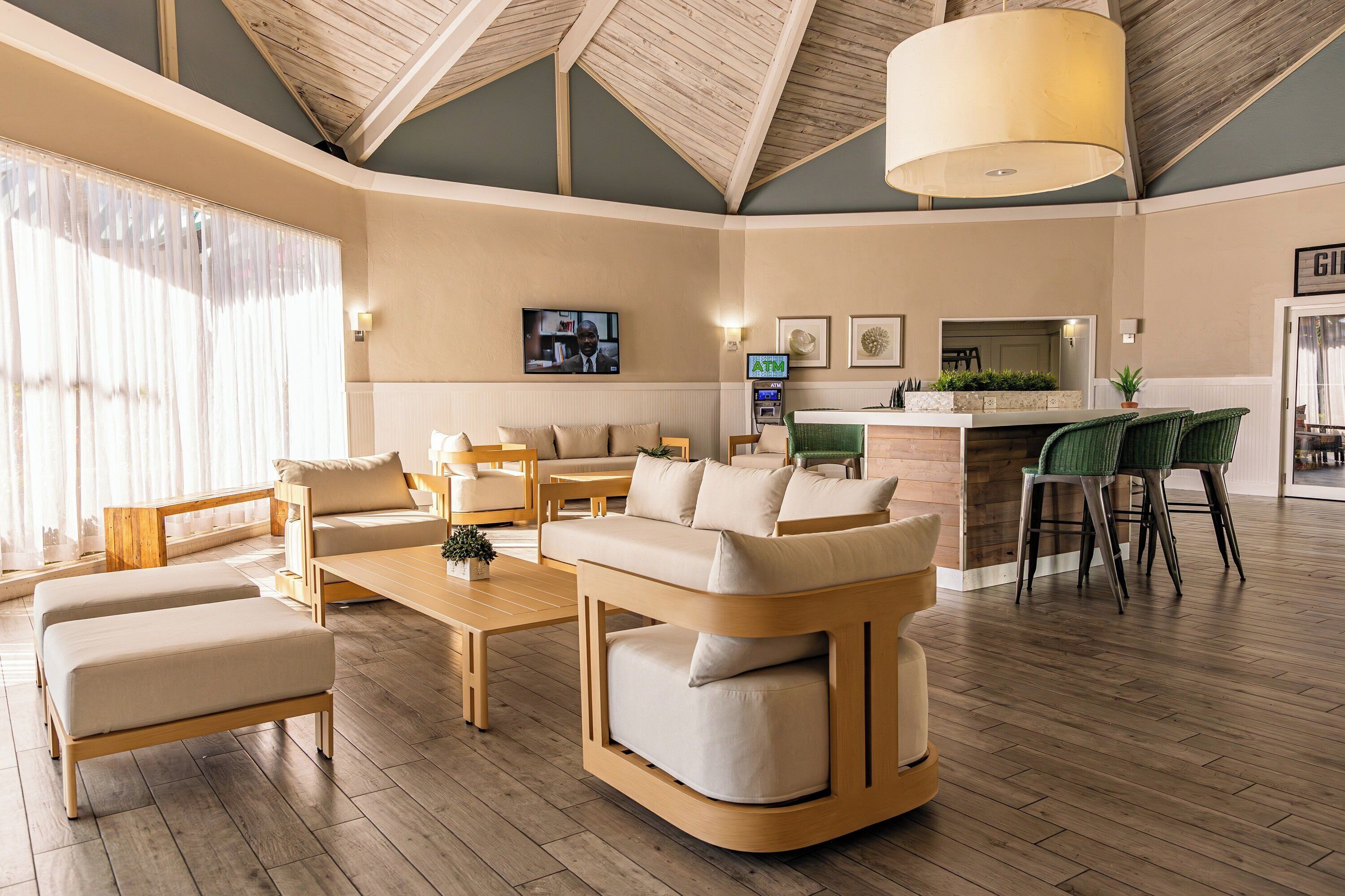 A spacious living area with a wooden ceiling, a sofa set, a coffee table, and a bar area with stools.