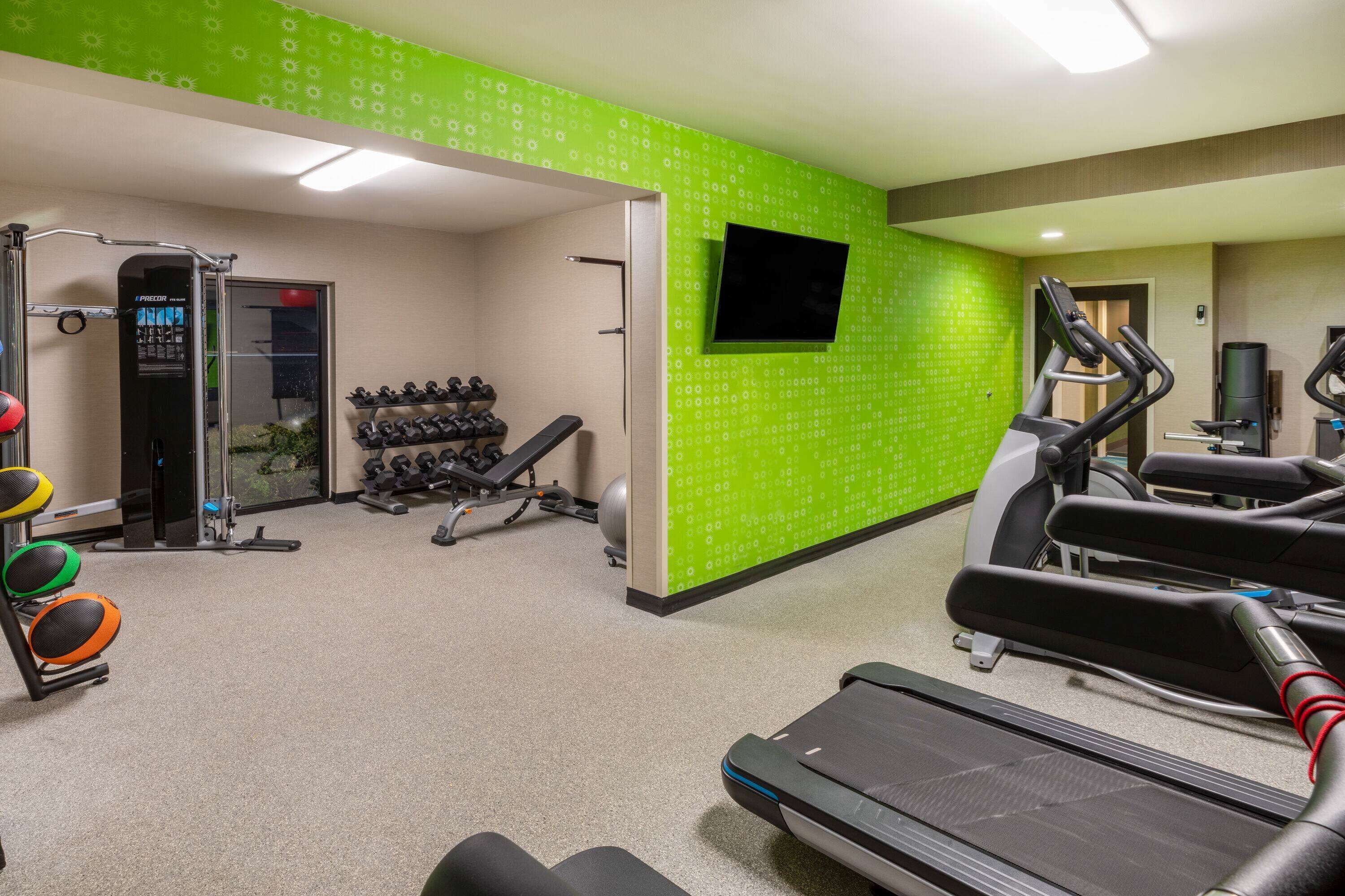 A gym with treadmills, dumbbells, and a TV on the wall.