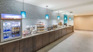 Un espace d’accueil moderne, typique d’un hôtel contemporain, avec un coin petit-déjeuner en libre-service comprenant un réfrigérateur rempli de boissons et une machine à café.