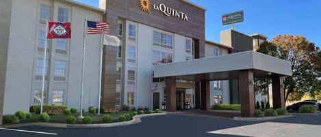 Un hotel con fachada moderna, un cartel llamativo de 'La Quinta' y un asta con la bandera estadounidense.