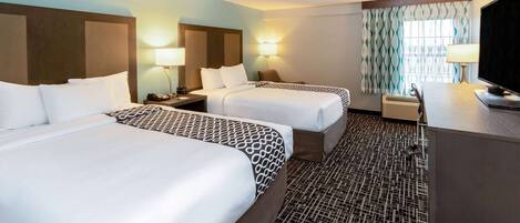 A hotel room with two beds, a desk, a TV, and a patterned carpet.