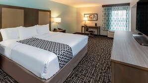 Une chambre d’hôtel avec un grand lit, un bureau, une chaise, une télévision et une fenêtre avec des rideaux à motifs.