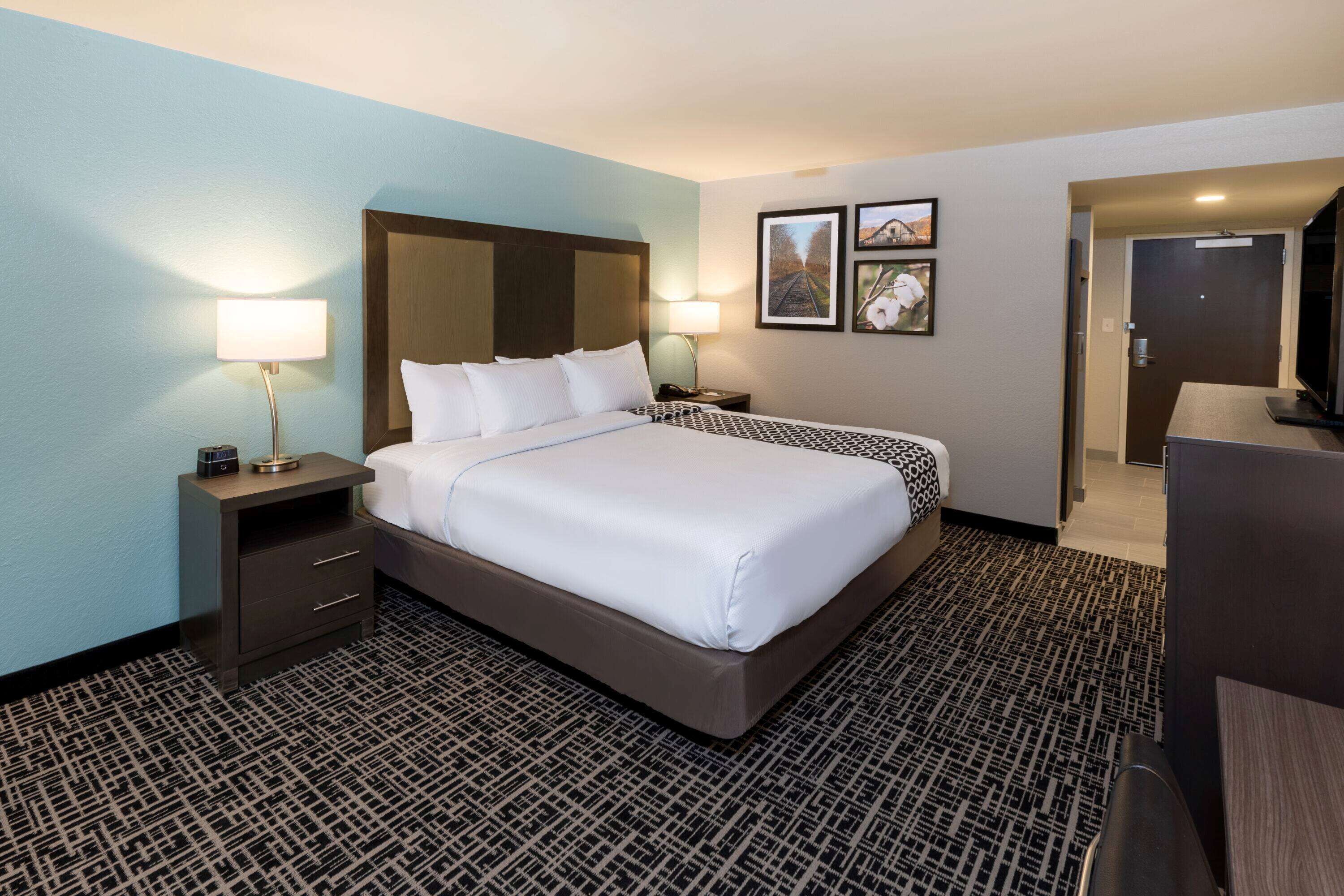 A hotel room with a large bed, two bedside tables with lamps, a TV, and framed pictures on the wall.