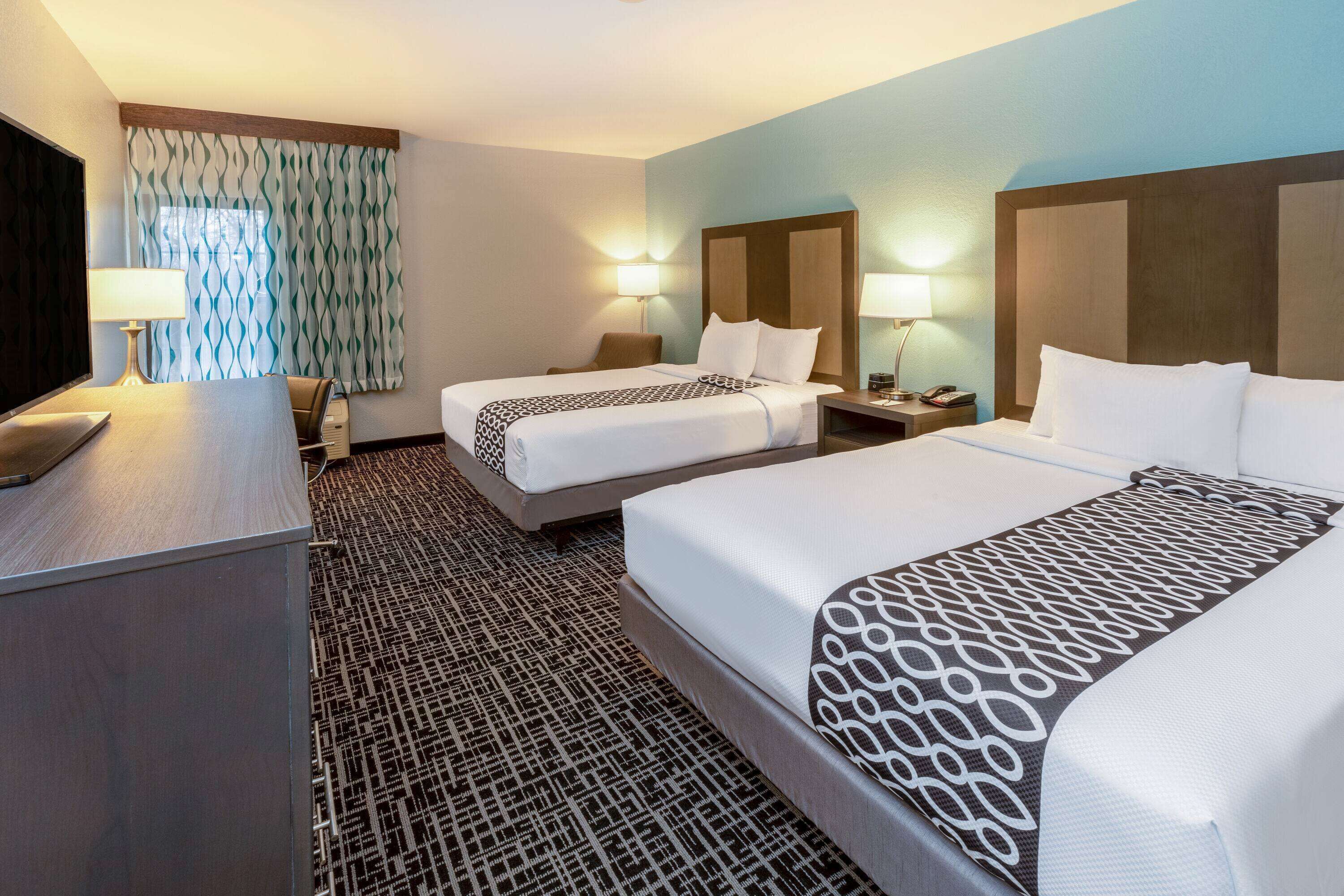 A hotel room with two beds, a desk, a TV, and two bedside lamps.