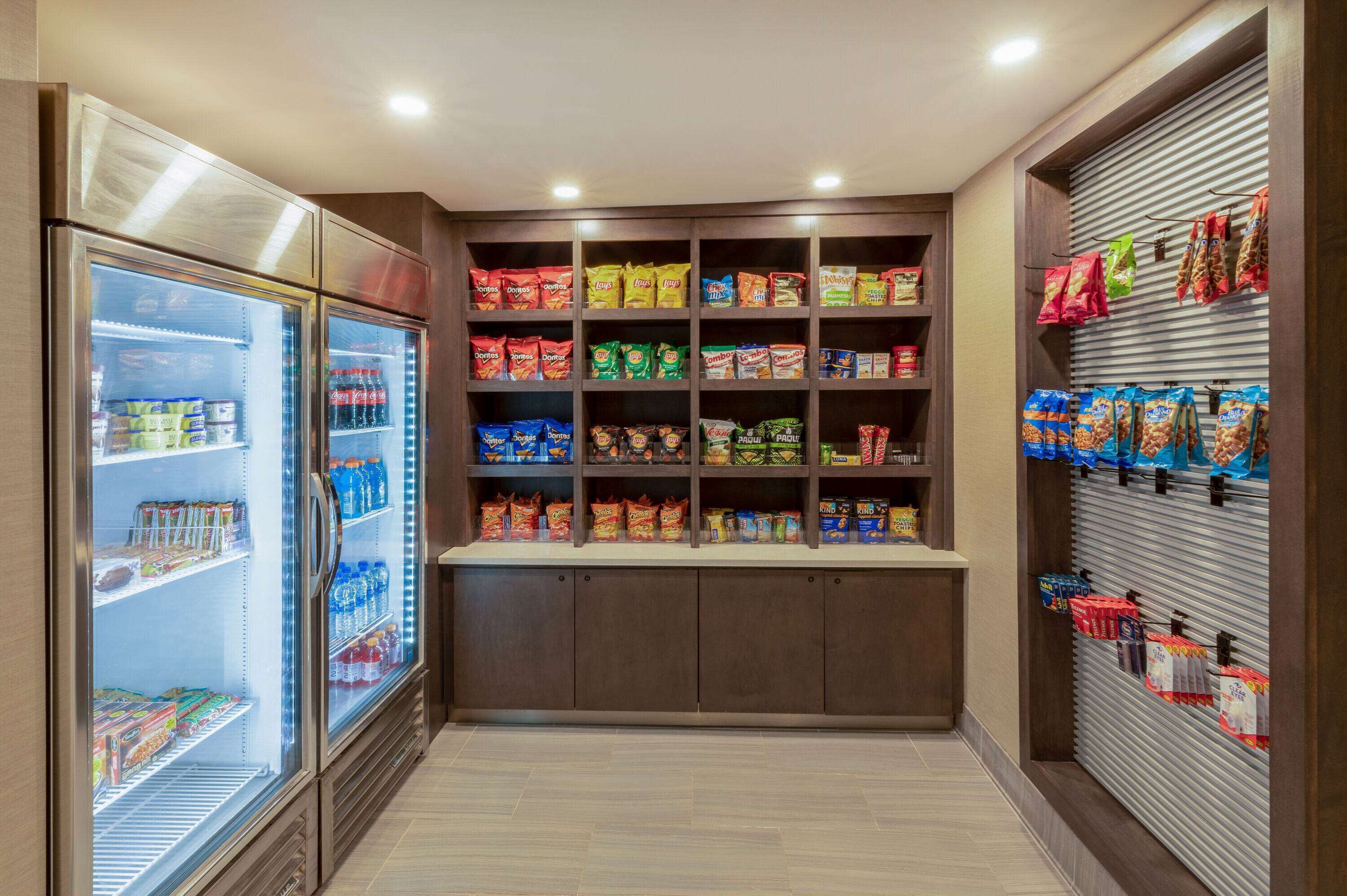 A well-lit storage room with shelves stocked with snacks and beverages, and a refrigerated section on the left.