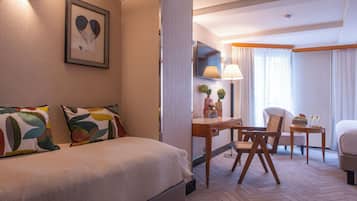 Habitación de hotel con cama, escritorio, silla, televisor y ventana con cortinas.