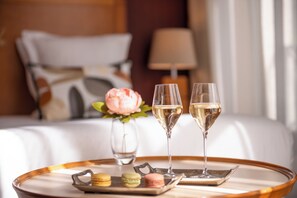 A neatly arranged tray with macarons and two glasses of champagne on a round table, set against a hotel room backdrop with a bed and a lamp. - Les Jardins du Marais (Paris)