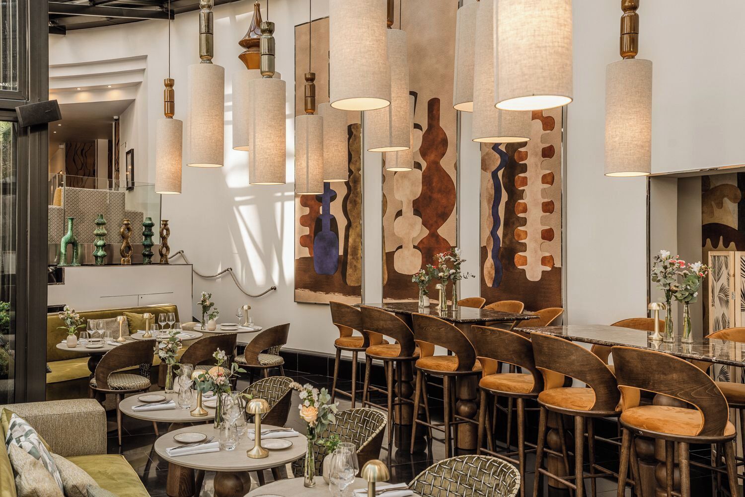 Interior de restaurante con mesas redondas, sillas, lámparas colgantes y arte abstracto en las paredes.