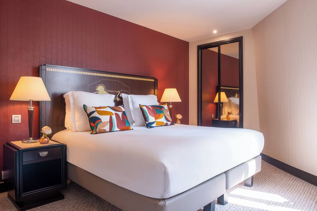 Ein Hotelzimmer mit einem großen Bett, zwei Nachttischen mit Lampen und einem Spiegel an der Wand.