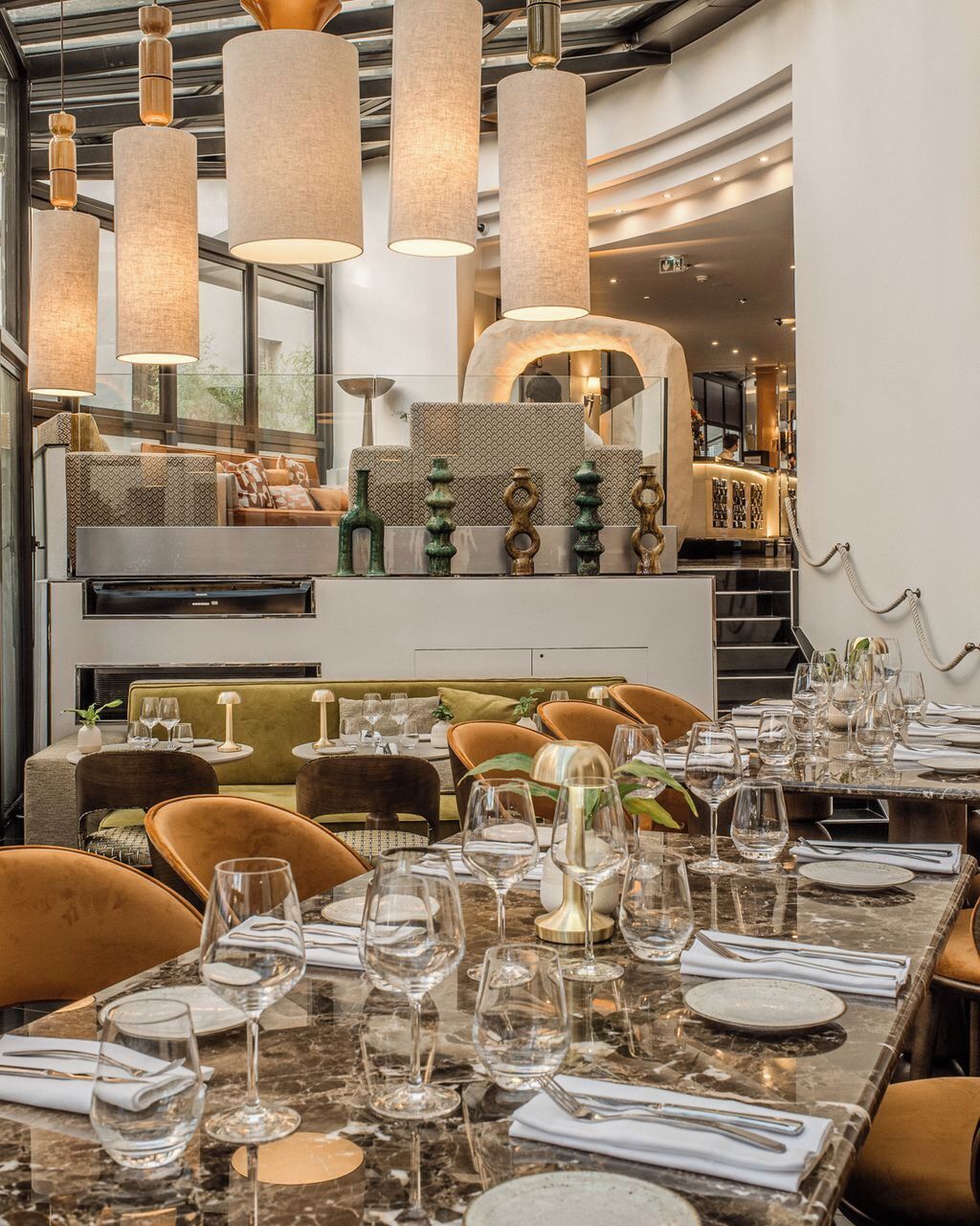 A restaurant interior with a long dining table, multiple chairs, and hanging pendant lights.