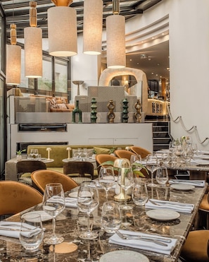Un interior de restaurante con una larga mesa de comedor, múltiples sillas y lámparas colgantes.