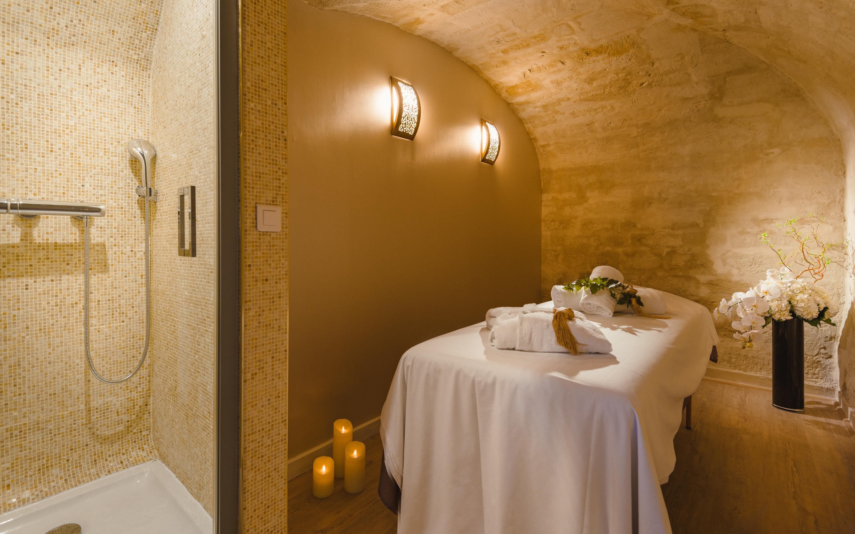 A bathroom with a shower, a bed with towels, candles, and a vase with flowers.