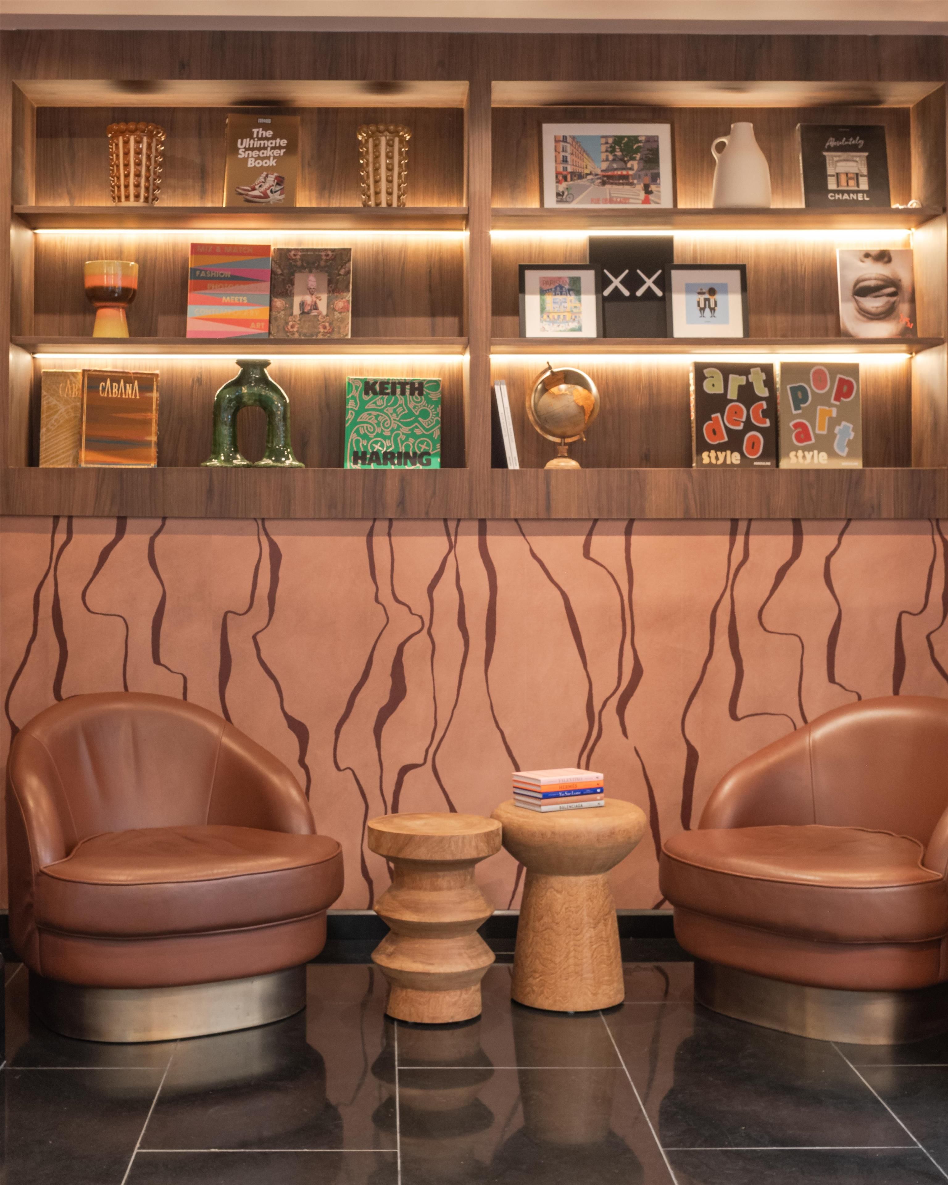 A reception area with leather chairs, a small wooden table, and a wall with shelves displaying books, a globe, and framed pictures.
