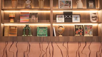 A reception area with leather chairs, a small wooden table, and a wall with shelves displaying books, a globe, and framed pictures.
