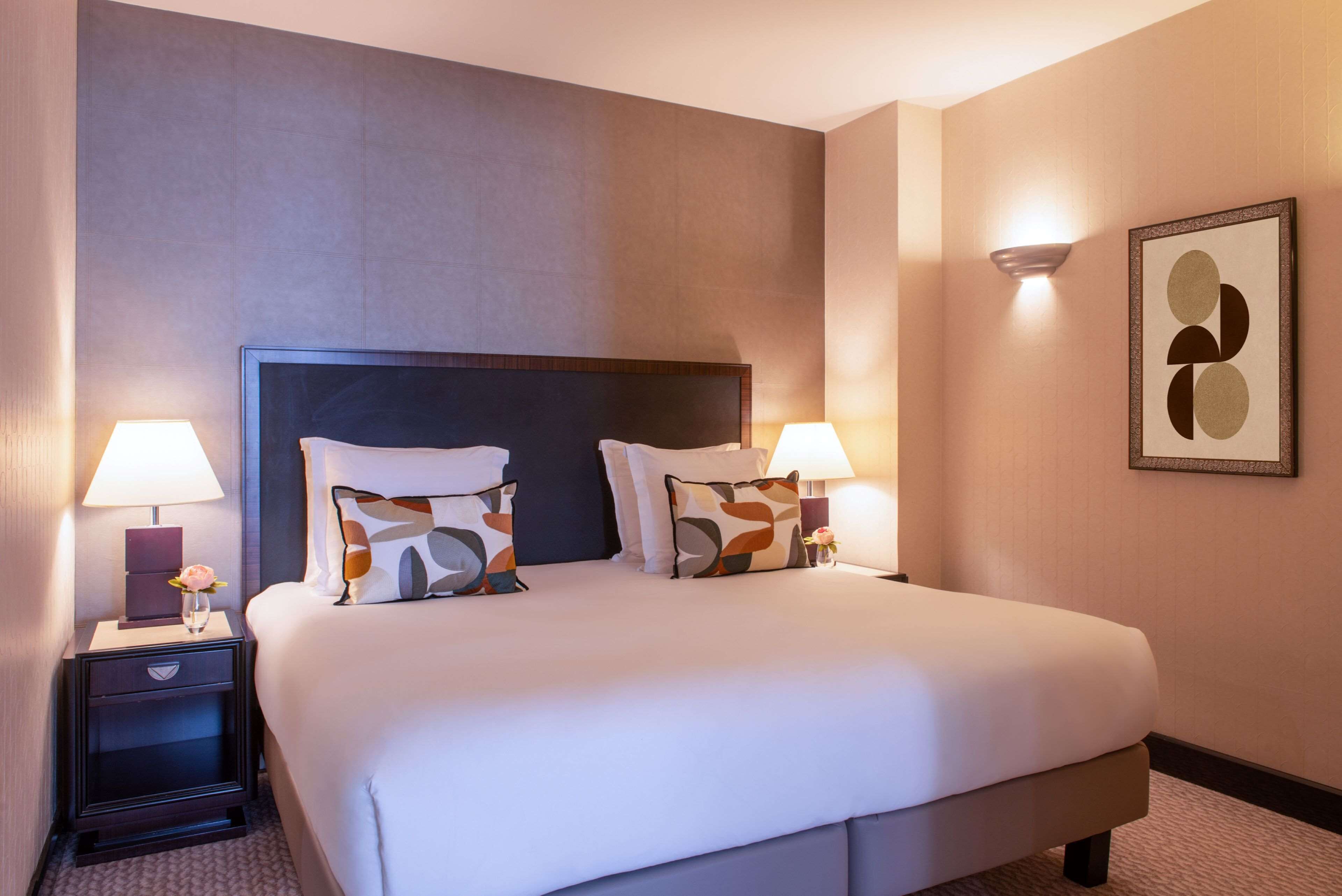 Habitación de hotel con una cama grande, dos mesitas de noche con lámparas y una obra de arte abstracta enmarcada en la pared.