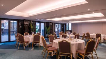 A conference room with round tables and chairs, large windows, and a carpeted floor.