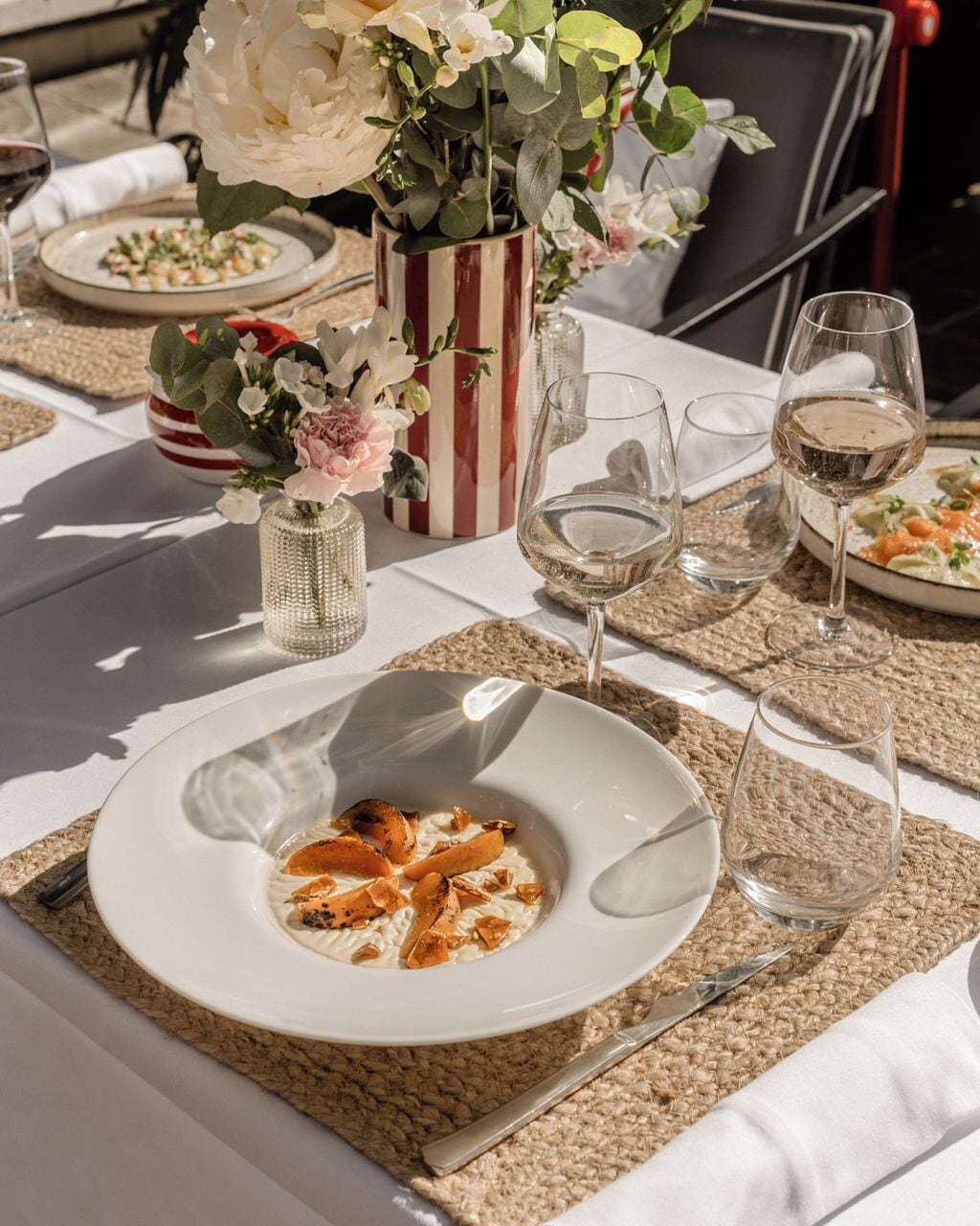 A table set with a plate of food, glasses of wine, and decorative flowers.