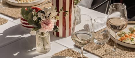 A table set with a plate of food, glasses of wine, and decorative flowers.