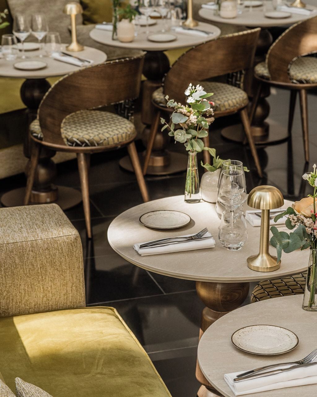 A dining area with round tables, chairs, and neatly set tables with plates, cutlery, and glassware.