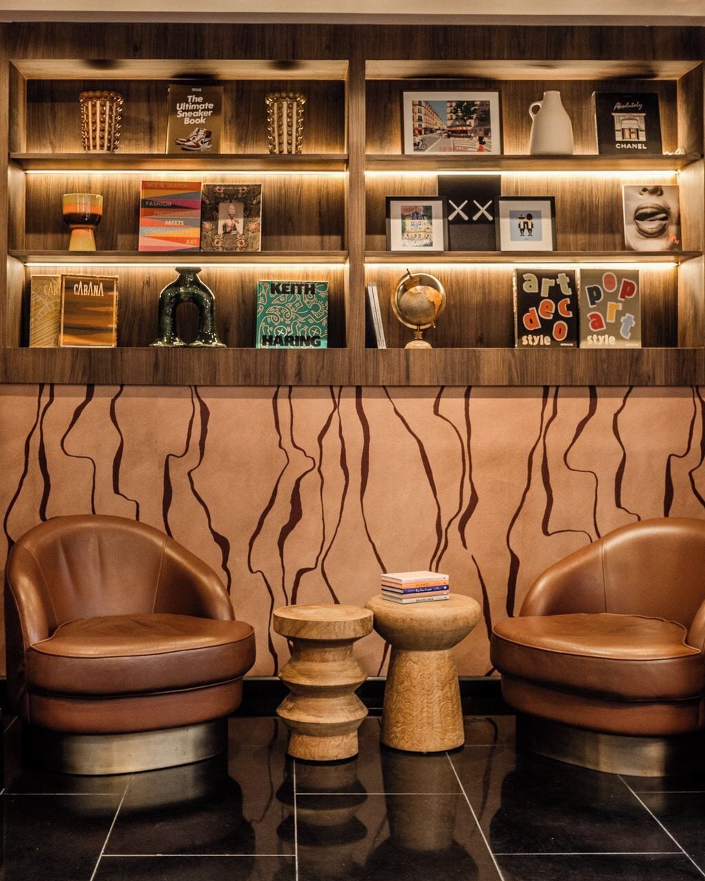 A lobby with leather chairs, a wooden wall with wavy patterns, and shelves with books and decorative items.