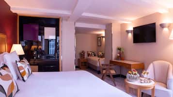 A hotel room with a bed, a desk, a chair, a TV, and a small table with drinks and snacks.