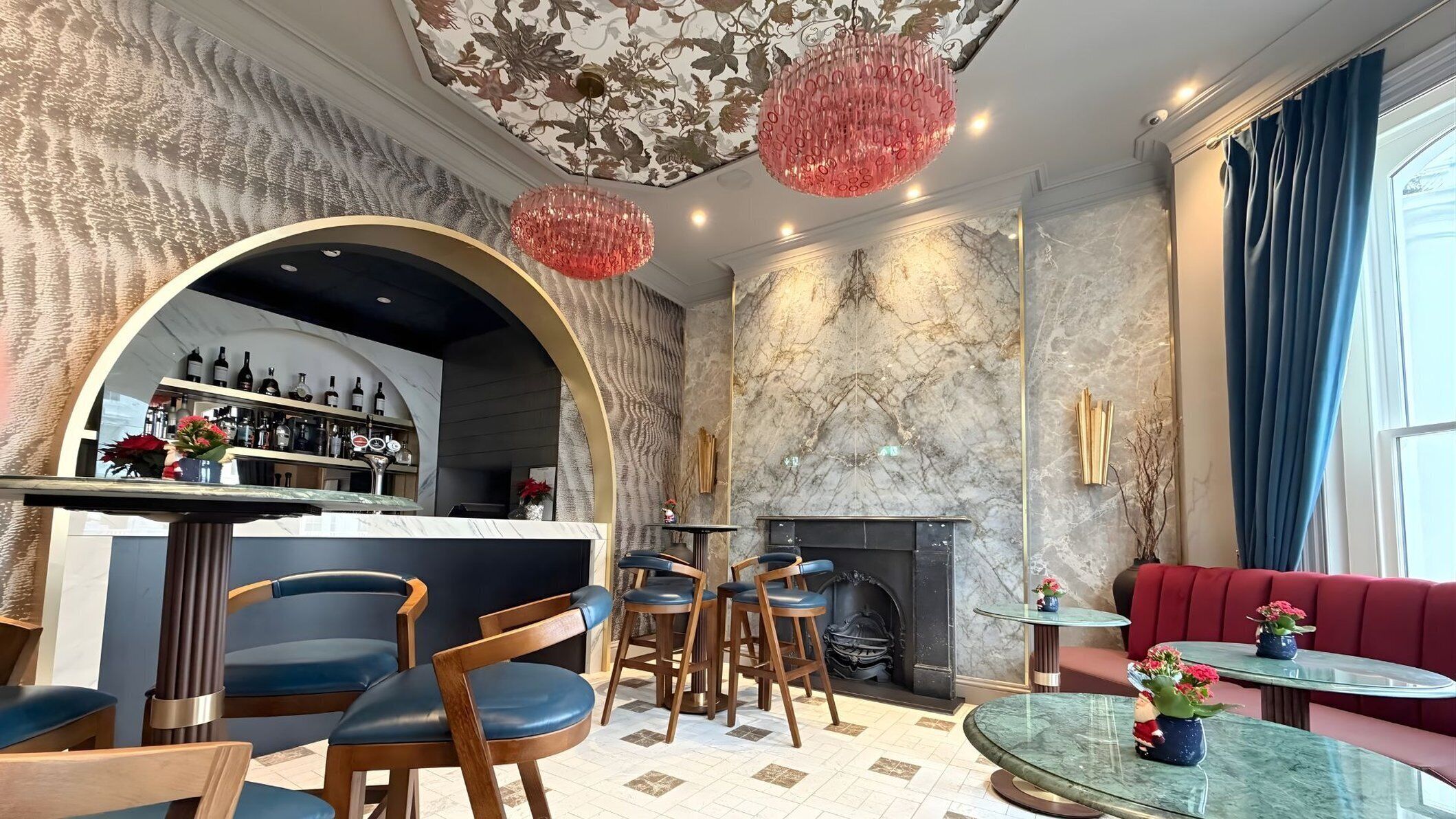 A bar area with a marble counter, wooden chairs, and a red sofa.
