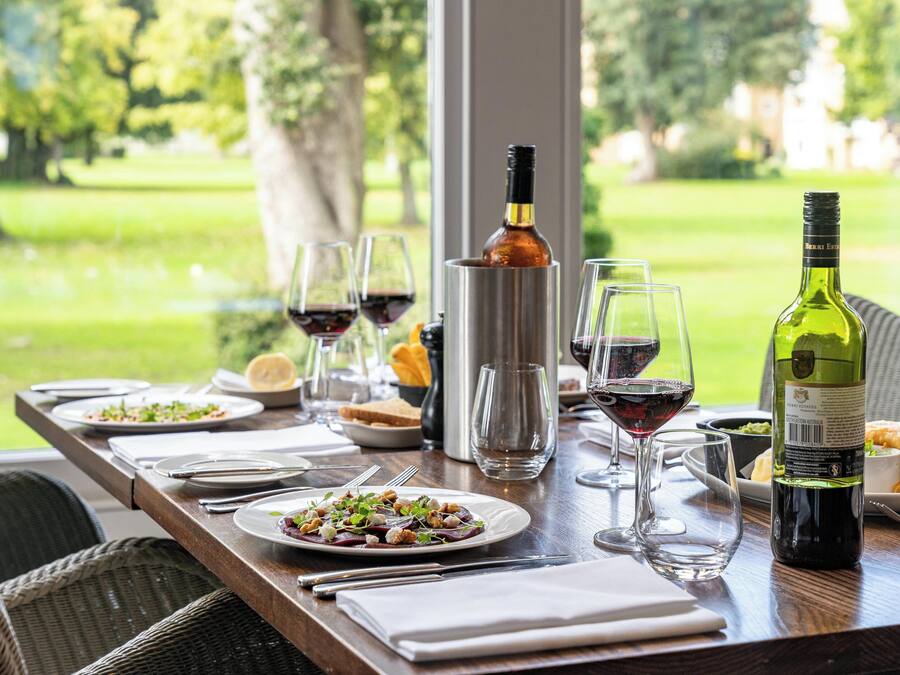 A dining table set with plates of food, wine glasses, and bottles of wine, overlooking a lush green landscape.