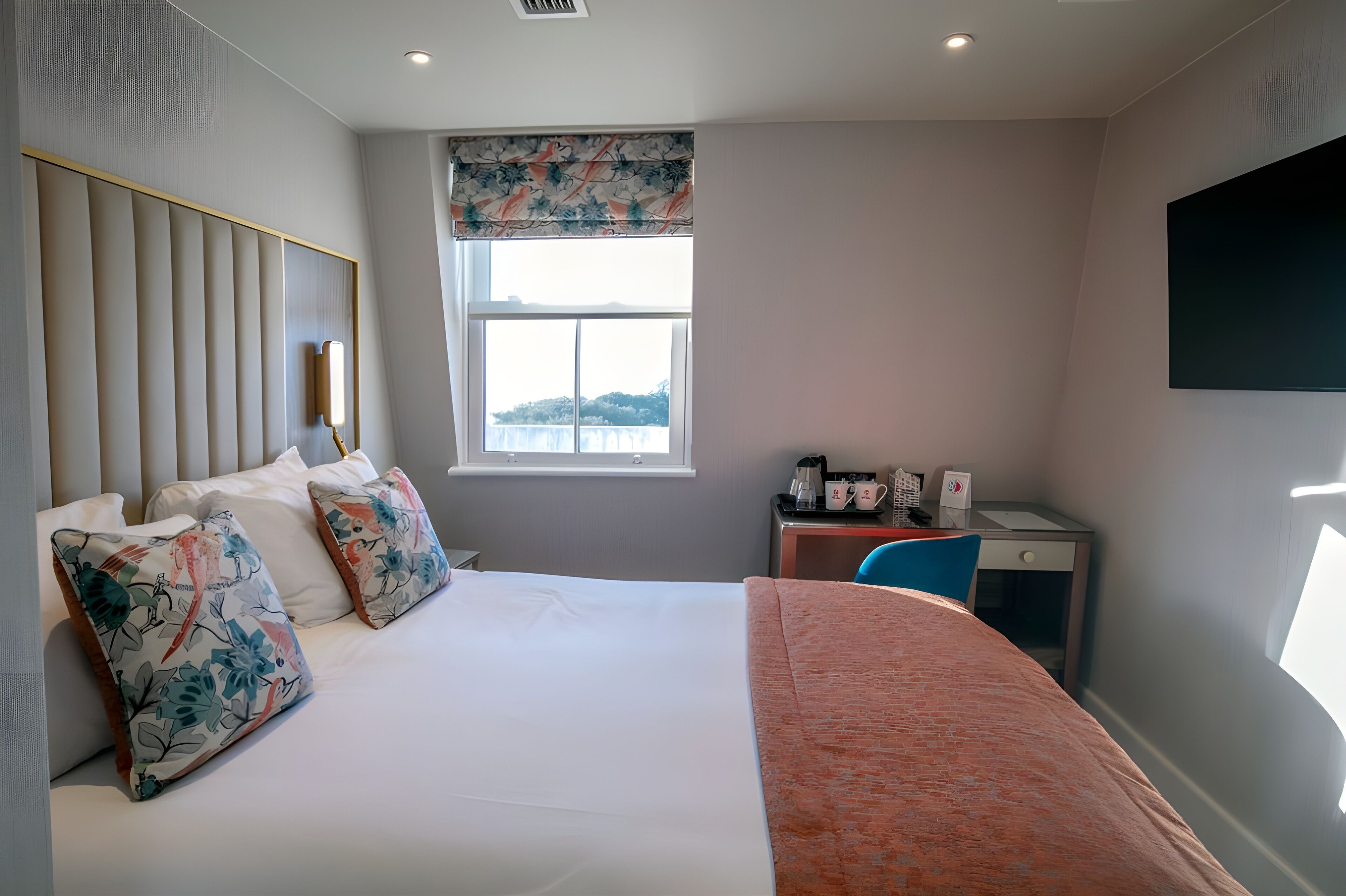 A hotel room with a bed, a desk, a chair, a window, and a television.