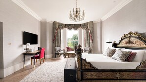 Ein Schlafzimmer mit einem großen Bett, einem Schreibtisch mit Stuhl, einem an der Wand befestigten Fernseher und einer Kandelaberleuchte.