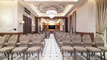 A hotel lobby with rows of chairs, a chandelier, and a television screen.