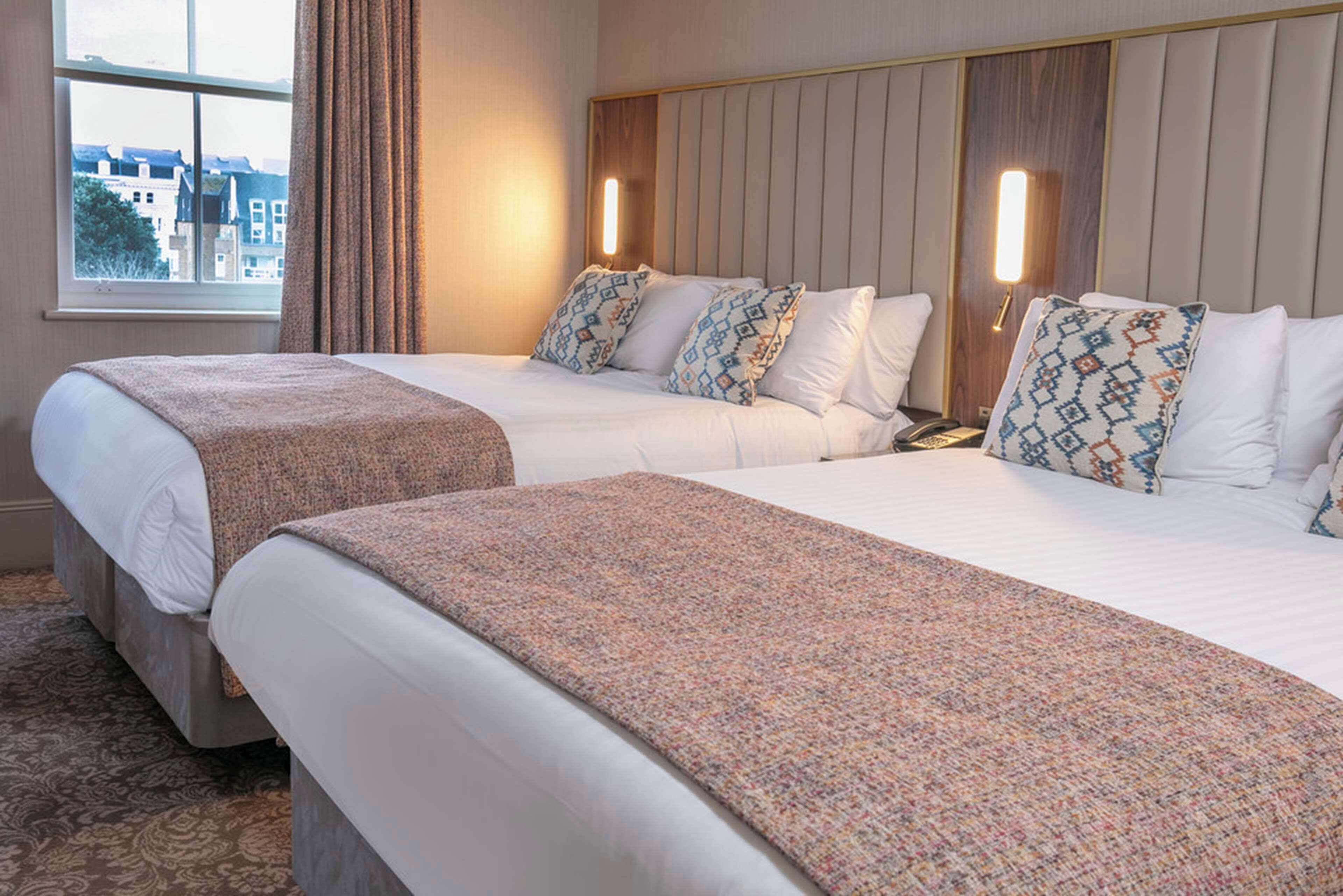 Habitación de hotel con dos camas, un ventanal grande y vistas de edificios.