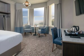 A hotel room with a bed, a desk with a kettle, two chairs, a small table, and a TV. - voco The Clifton Folkestone by IHG (Folkestone)