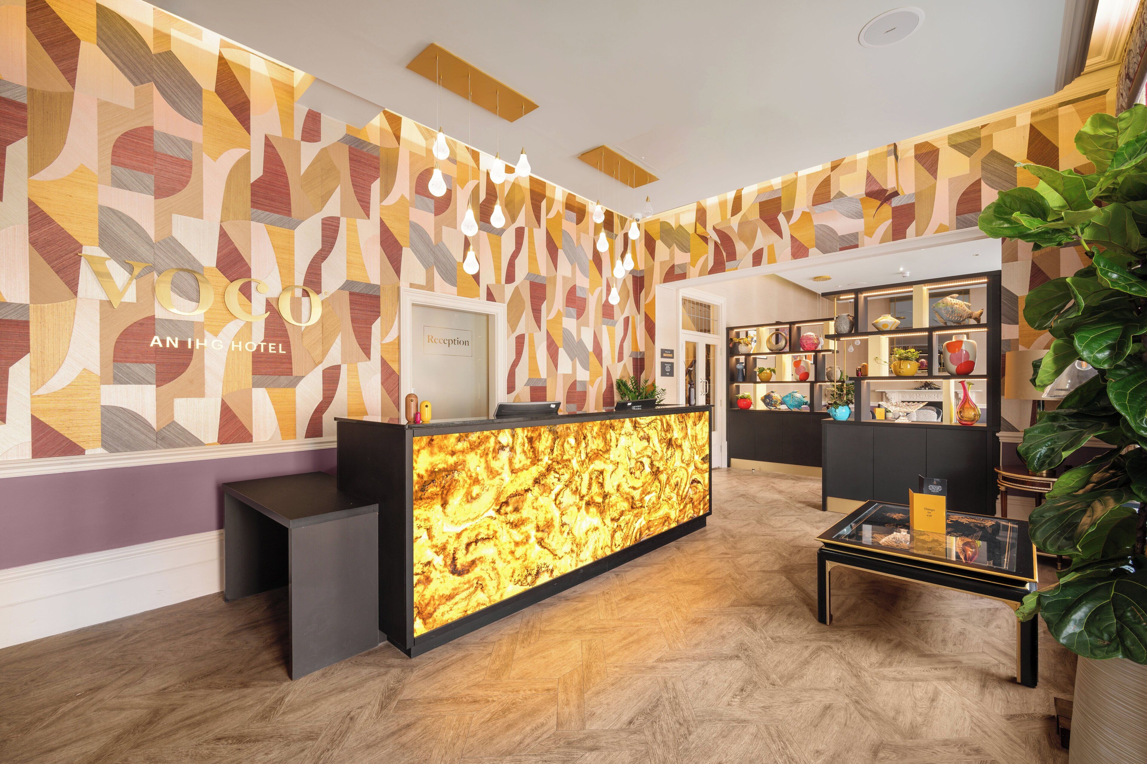 A reception desk with a geometric patterned wall, a reception area, and a seating area with a coffee table.