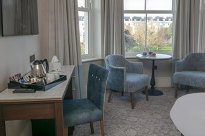 A hotel room with a desk, two chairs, a small table, and a view of buildings and trees outside. - voco The Clifton Folkestone by IHG (Folkestone)