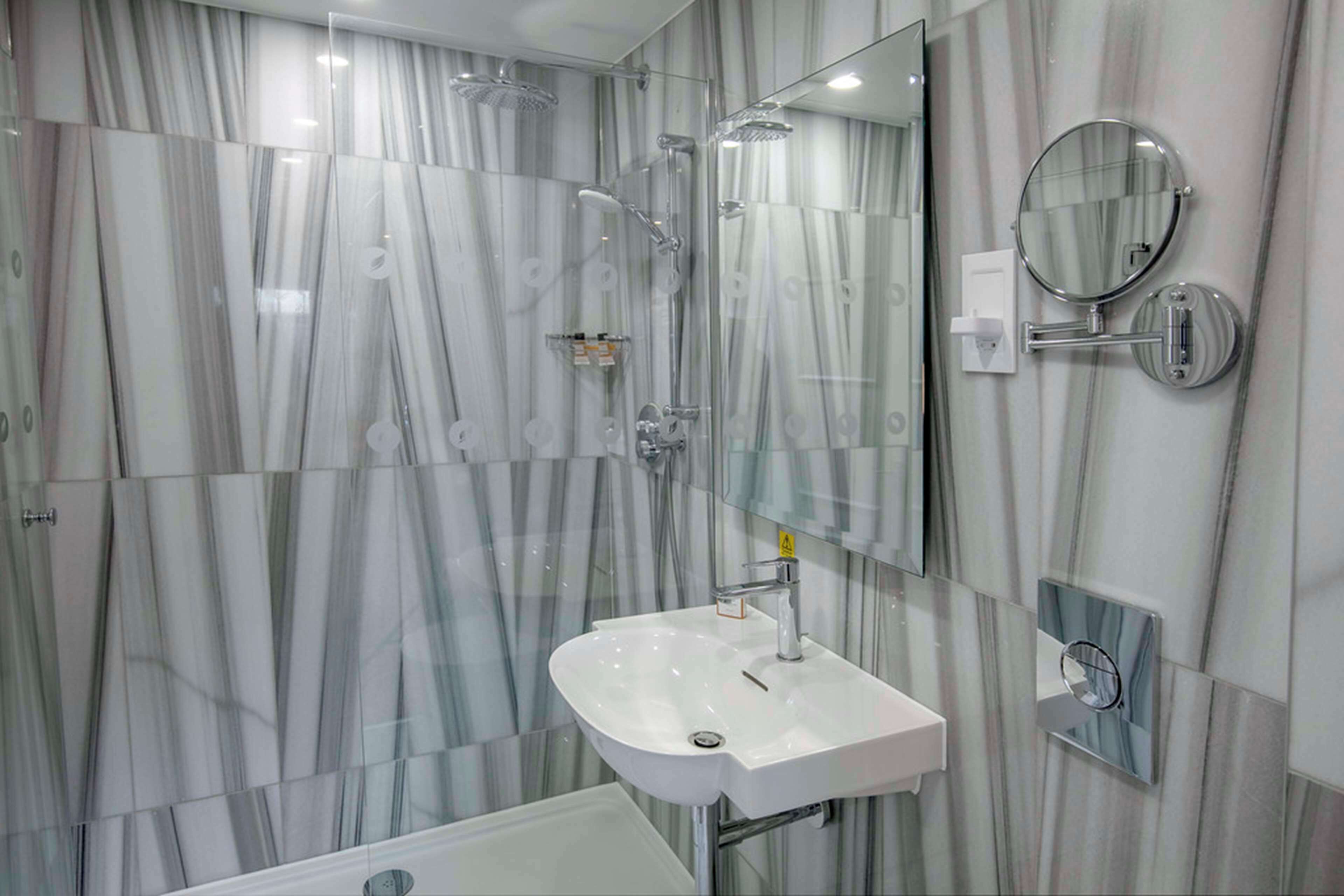 Un bagno moderno con cabina doccia in vetro, lavandino bianco e specchio.